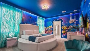 Un dormitorio con una cama redonda, un sillón color turquesa y un mural de una escena submarina.