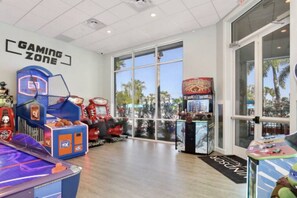 Un'area giochi con cabinati arcade, canestro da basket e un'ampia vetrata vista palme.