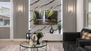 Un salon moderne doté d’un grand téléviseur à écran plat fixé sur un mur en marbre, d’un canapé en cuir noir et d’une table basse en verre agrémentée d’objets décoratifs.