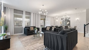 Un salon moderne avec un canapé, une table basse et un coin repas agrémenté d’un lustre.