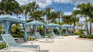 A poolside area with lounge chairs and umbrellas, surrounded by palm trees and a clear sky. - Disney| Solara Resort Pool & Spa (Kissimmee)