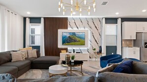 A modern living room with a sectional sofa, a round coffee table, and a flat-screen TV mounted on the wall. - Disney| Solara Resort Pool & Spa (Kissimmee)
