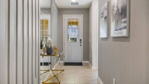 A hallway with a white door, a small table with a vase, and two framed pictures on the wall. - Disney| Solara Resort Pool & Spa (Kissimmee)