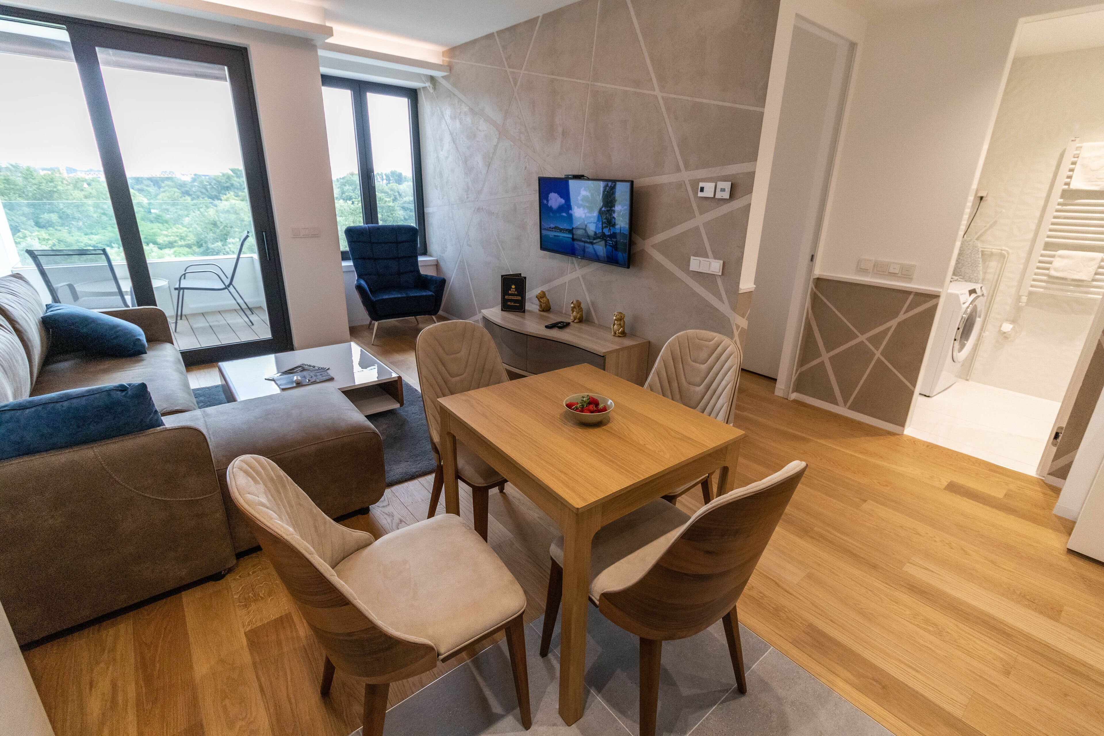 Un salon moderne avec une table à manger en bois, des canapés de couleur beige et un téléviseur fixé au mur.