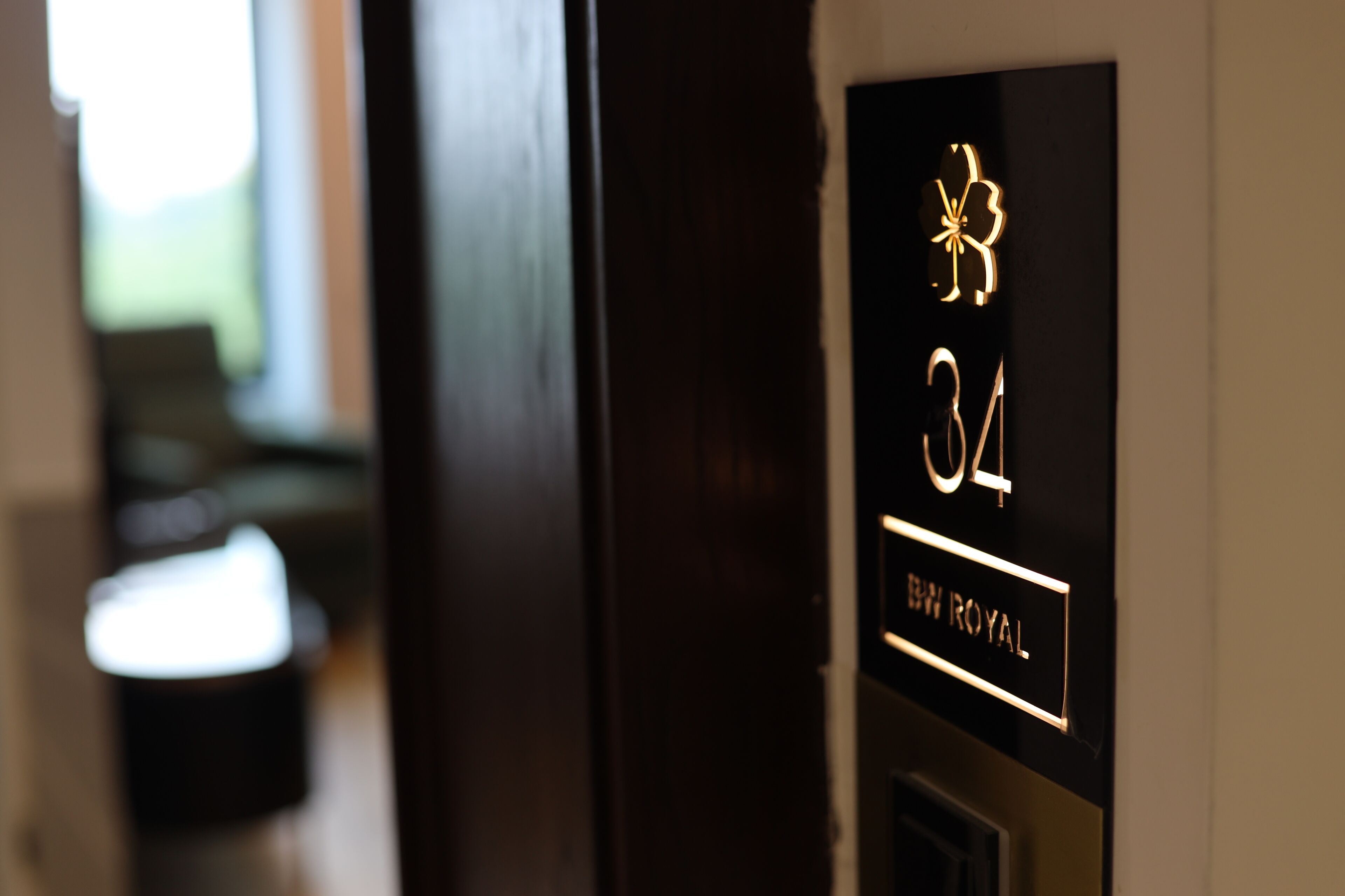 Un primer plano del cartel de número de habitación de un hotel, con un emblema decorativo y la inscripción 'BW ROYAL'.