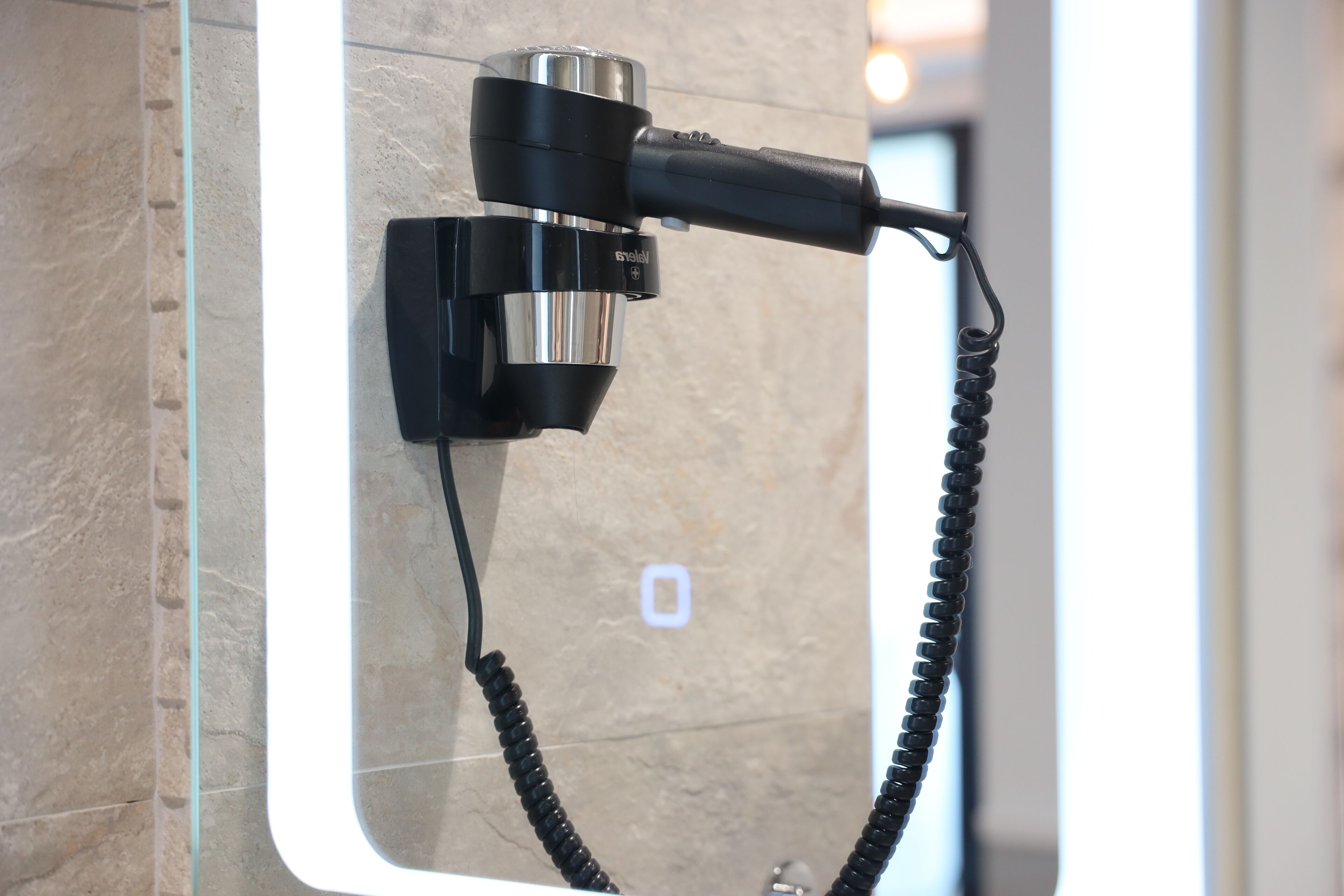 A hairdryer mounted on a wall with a cord.