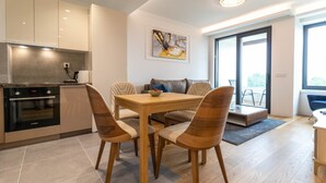 Une cuisine moderne dotée d’un four encastré, un coin repas avec une table et des chaises en bois, et une grande fenêtre offrant une vue sur l’extérieur.