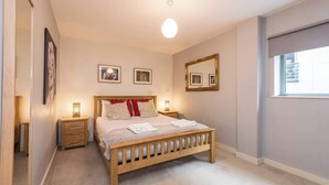 A bedroom with a wooden bed, bedside lamps, a large mirror, and framed pictures on the wall. - Host & Stay | York Place Apartment (Liverpool)