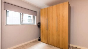 A room with a large wooden wardrobe, a window with blinds, and a wall-mounted fan. - Host & Stay | York Place Apartment (Liverpool)