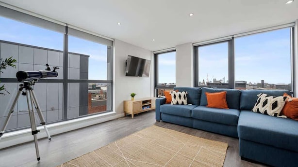 A modern living room with a large window, a sofa, a telescope, and a flat-screen TV.