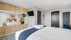 A modern hotel room with a large bed, a TV mounted on the wall, a wardrobe, and a door with a curtain.