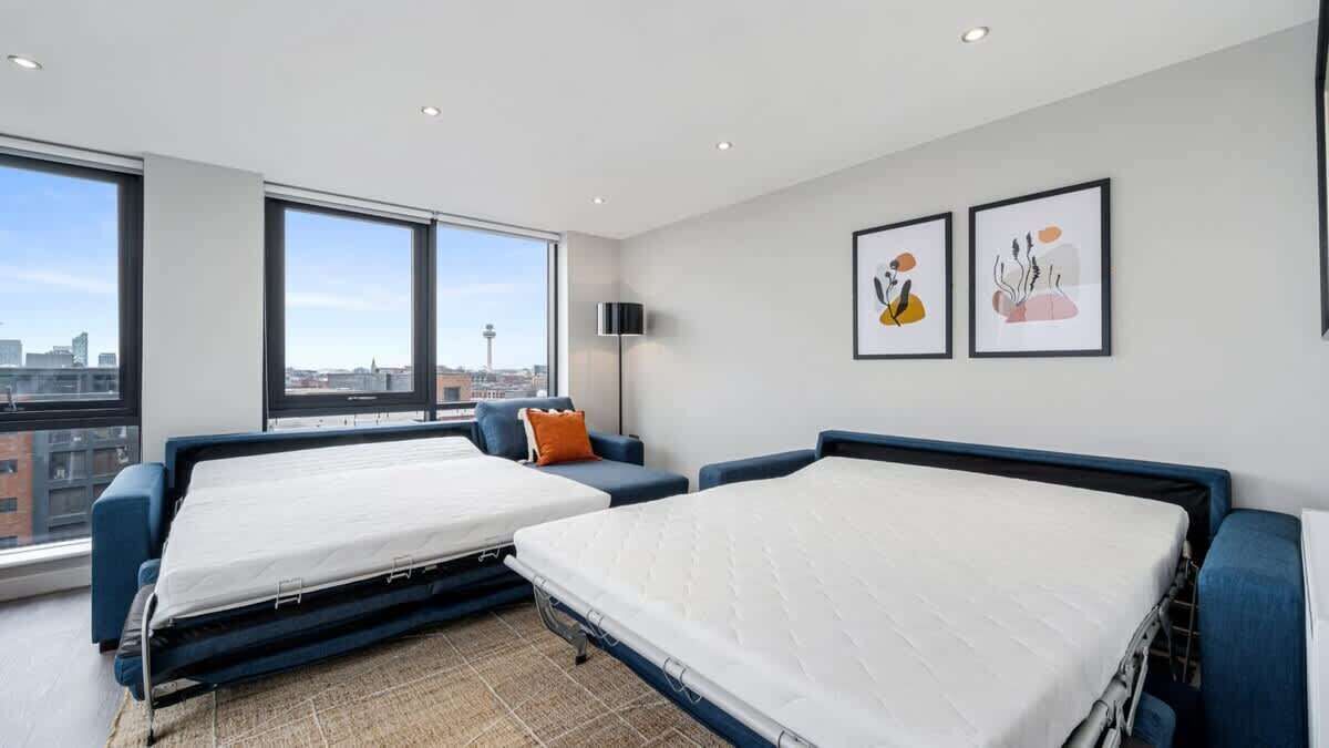 Habitación de hotel moderna con dos camas, un ventanal amplio con vistas a la ciudad y dos cuadros enmarcados en la pared.