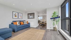 A modern living room with a blue sofa, a dining area, and a telescope on a tripod.