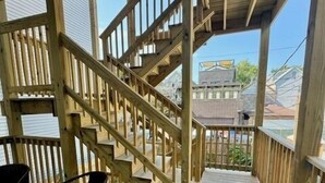 Une terrasse en bois avec un escalier menant à un niveau supérieur, agrémentée d’une rambarde et de deux chaises.