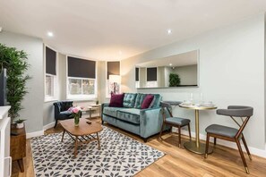 A modern living room with a teal sofa, a round coffee table, and a dining area with a small table and chairs.
