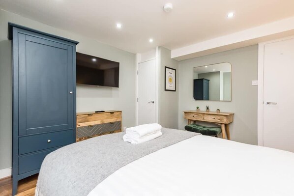 A bedroom with a bed, a wardrobe, a vanity with a mirror, and a framed certificate on the wall.