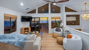 A spacious living area with a large TV, comfortable seating, and a balcony with ocean views.