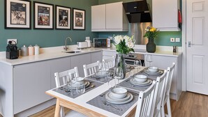 Una cocina moderna con armarios blancos, una mesa de comedor para seis personas y carteles enmarcados de los Beatles en la pared.