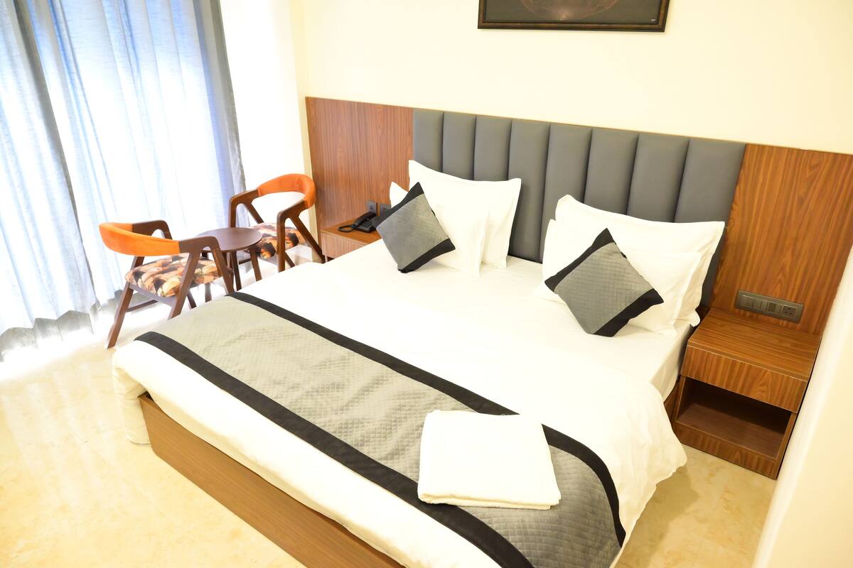 A neatly made bed with a grey headboard, a bedside table with a phone, and a chair.