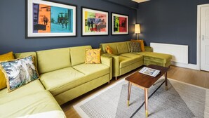 Ein Wohnzimmer mit einem grünen Sofagarnitur, einem Couchtisch und gerahmten Kunstwerken an der Wand.