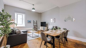 Een moderne woonkamer met een bank, een eettafel, stoelen, een televisie en een potplant.