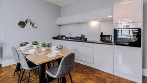 Een moderne keuken met witte kasten, een inbouwoven en een eethoek met een houten tafel en grijze stoelen.