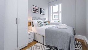 Een slaapkamer met een bed, een kledingkast, een raam en twee foto's in lijsten aan de muur.
