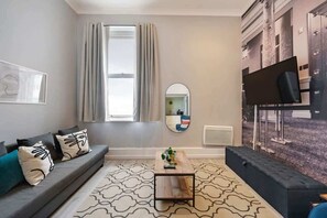 Een moderne woonkamer met een bank, salontafel, spiegel en een groot raam met gordijnen.