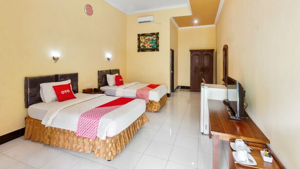 A hotel room with two beds, a TV, a desk with a computer, and a small table with a tray. - Capital O 93391 Golden Manggis Hotel Near SMKN 1 Lingsar (Batu Kumbung)