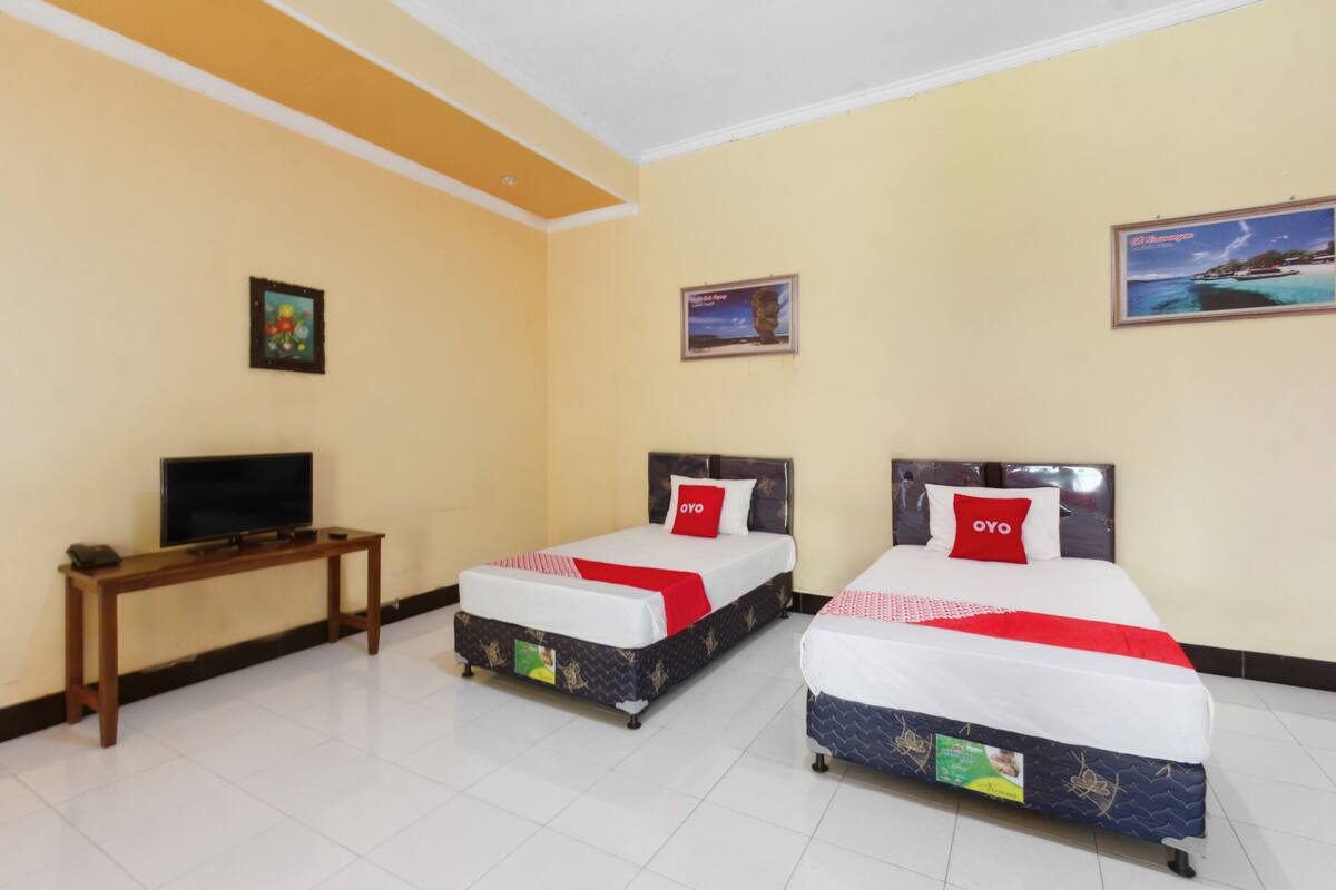A hotel room with two beds, a TV on a wooden table, and a framed picture on the wall.