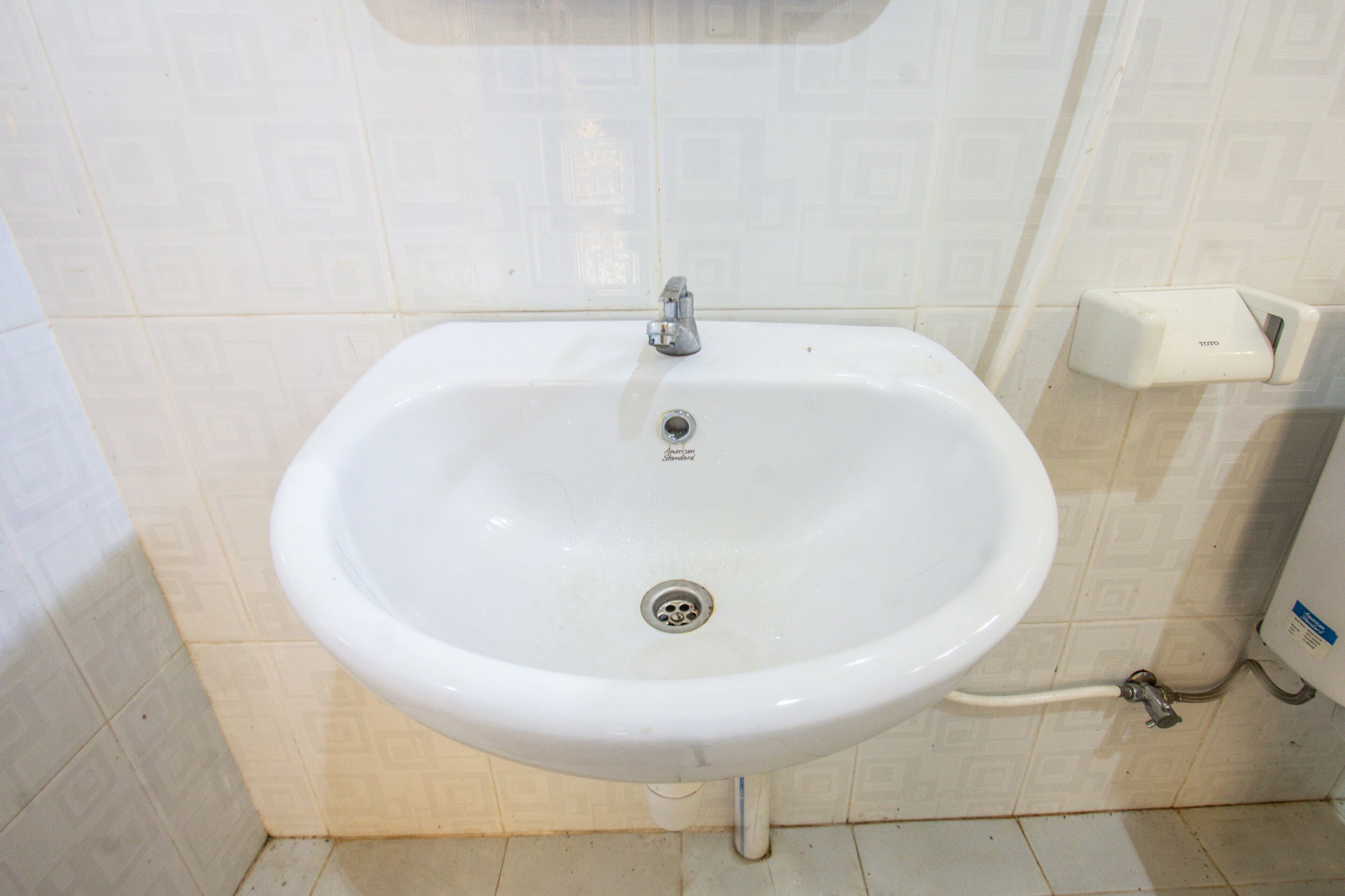 A white bathroom sink with a single faucet, a drain, and a soap dispenser on the wall.