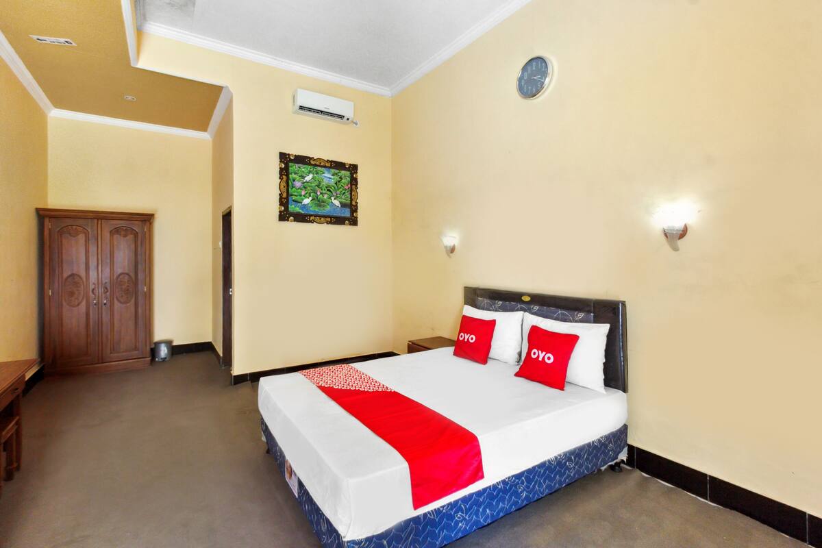A hotel room with a bed, a wardrobe, a small table, and a wall clock.