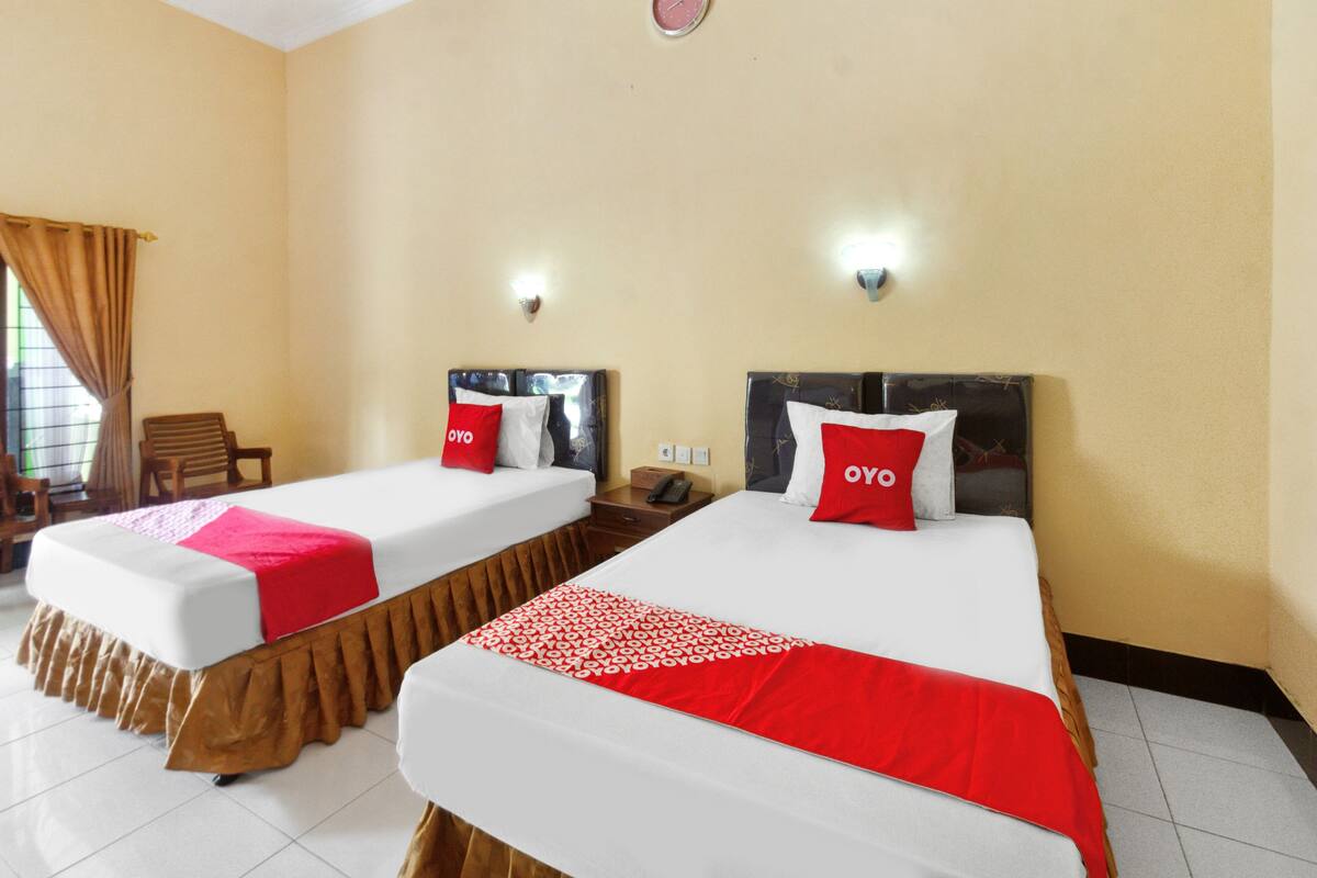 A hotel room with two beds, each with a red and white blanket, and a red pillow with the logo "OYO".