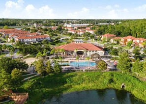 Surrounded by lush greenery and palm trees, this resort features a central building with a swimming pool and stucco walls.
