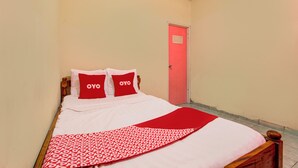 En säng för en person med en träram, vita sängkläder och röda kuddar med ordet ”OYO” på.