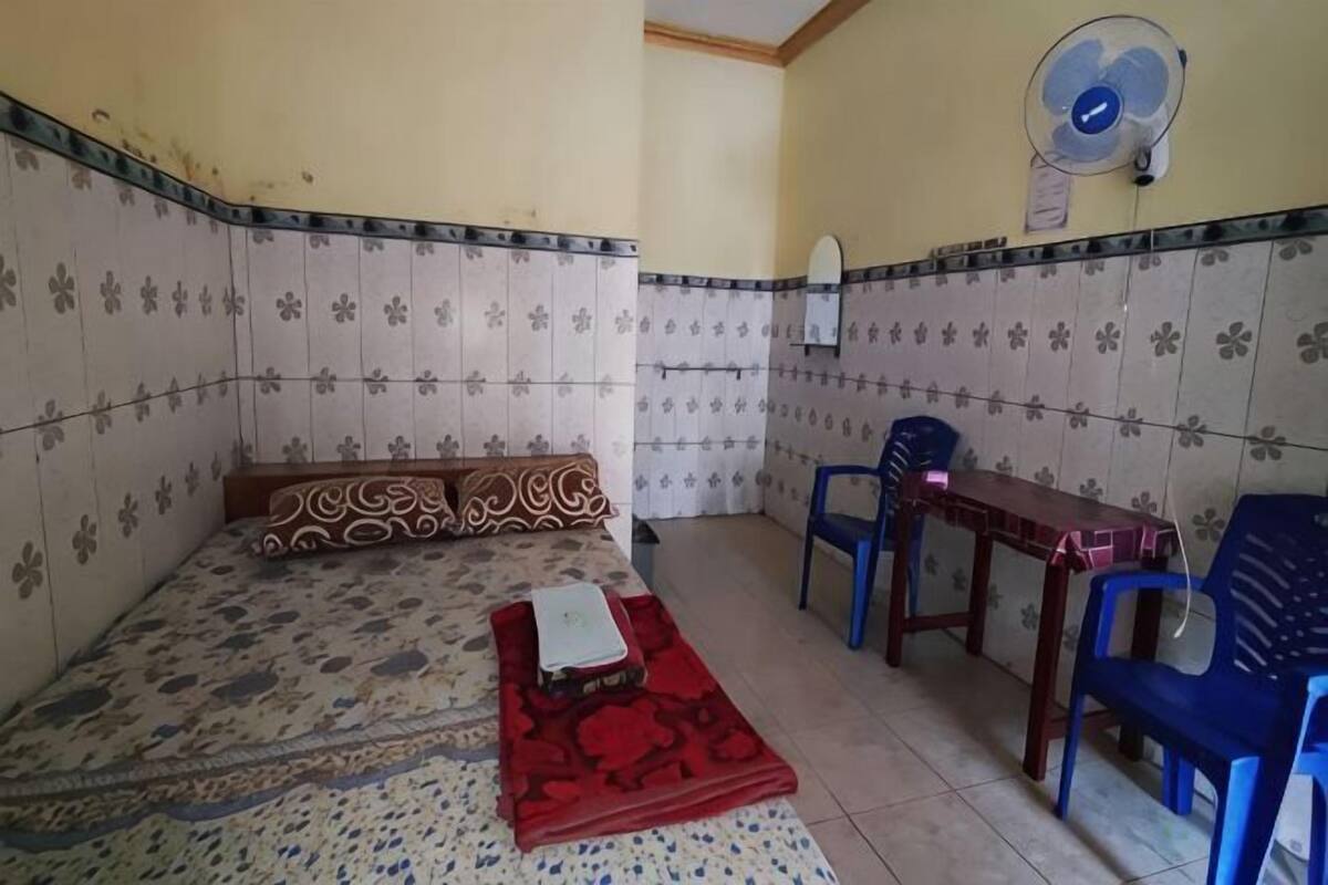 Una habitación con una cama, una mesa, dos sillas, un ventilador y un espejo en la pared.