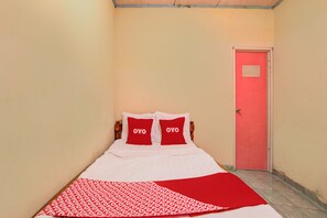 Una cama individual con dos almohadas, una manta estampada y una puerta con un cartel.