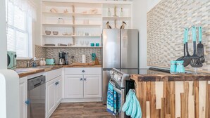 Una cocina con armarios blancos, encimera de madera, refrigerador de acero inoxidable y salpicadero de azulejos.