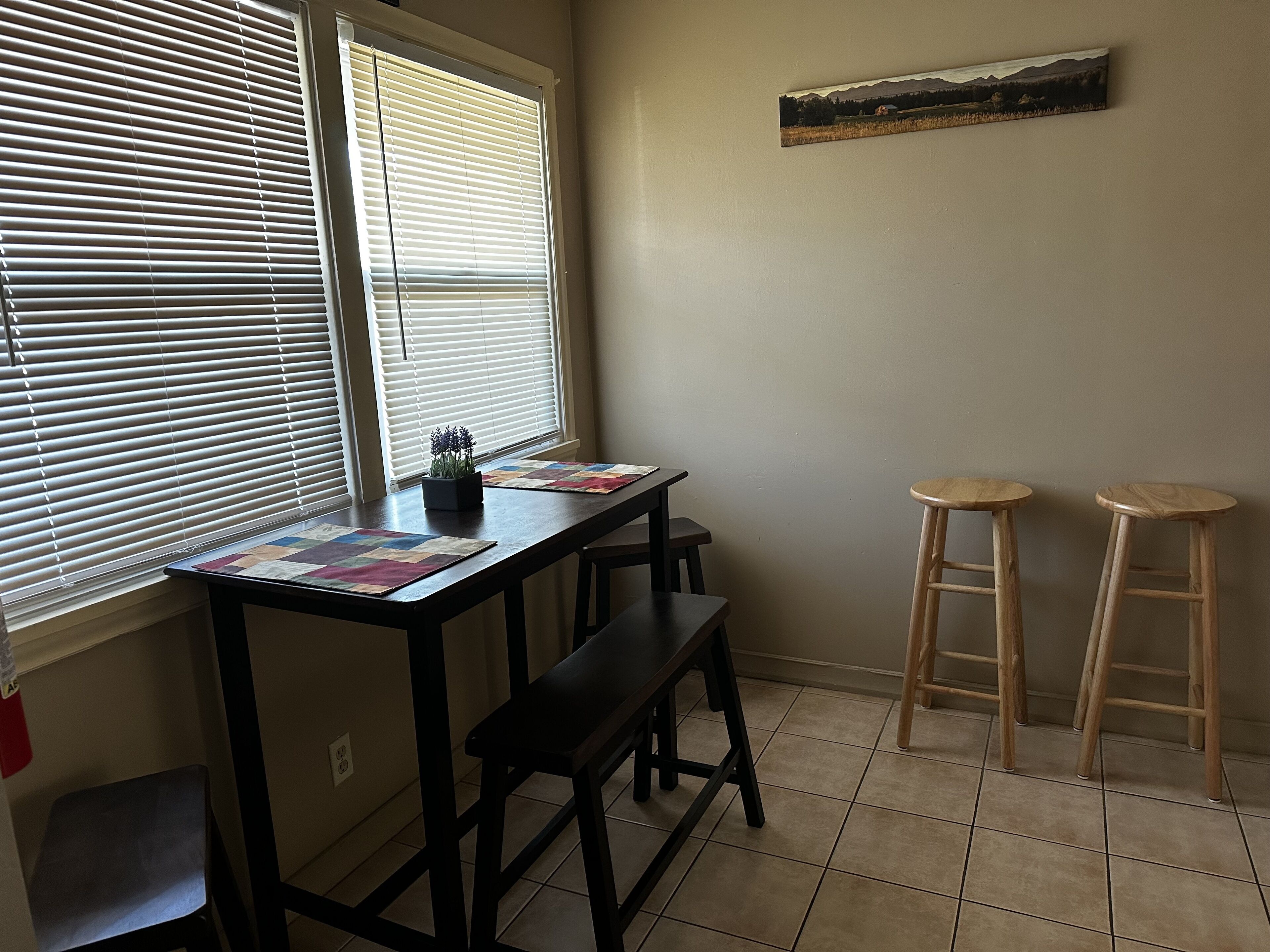 A room with a desk, two stools, and a window with blinds.