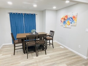 A dining area with a wooden table and chairs, a blue curtain, and a colorful abstract painting on the wall. - Waterfront 3BR Home | Lake Views & Kayak Launch (Reidsville)