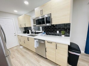 A modern kitchen with light wood cabinets, a stainless steel microwave, and a dishwasher. - Waterfront 3BR Home | Lake Views & Kayak Launch (Reidsville)