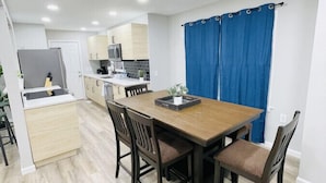 A modern kitchen with white cabinets, a wooden dining table, and blue curtains. - Waterfront 3BR Home | Lake Views & Kayak Launch (Reidsville)
