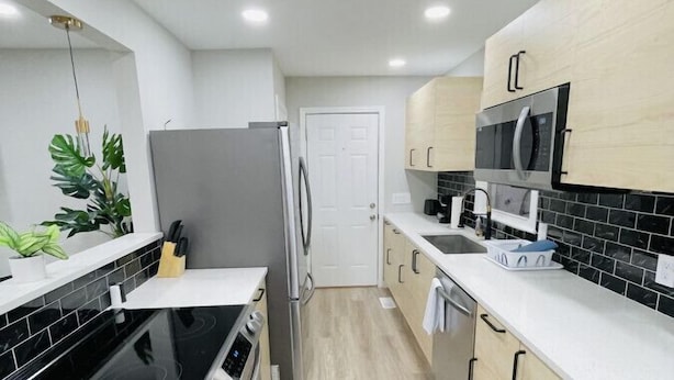 A modern kitchen with a black stovetop, stainless steel refrigerator, and white cabinetry. - Waterfront 3BR Home | Lake Views & Kayak Launch (Reidsville)