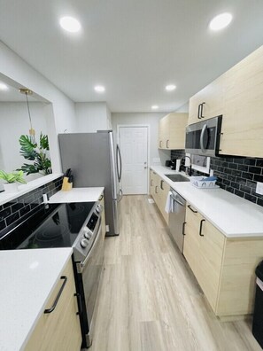 A modern kitchen with a black stovetop, stainless steel refrigerator, and white cabinetry.
