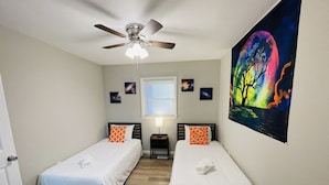 A bedroom with two single beds, a ceiling fan, a window with blinds, and a wall-mounted painting. - Waterfront 3BR Home | Lake Views & Kayak Launch (Reidsville)