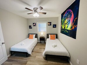 A bedroom with two single beds, a ceiling fan, a window with blinds, and a wall-mounted painting. - Waterfront 3BR Home | Lake Views & Kayak Launch (Reidsville)