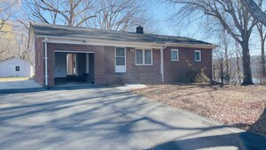 A single-story brick building with a garage entrance, a small porch, and a clear sky. - Waterfront 3BR Home | Lake Views & Kayak Launch (Reidsville)