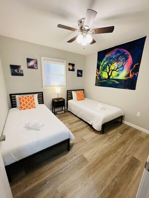 A bedroom with two beds, a ceiling fan, a nightlight, and a painting of a tree by a moonlit lake. - Waterfront 3BR Home | Lake Views & Kayak Launch (Reidsville)