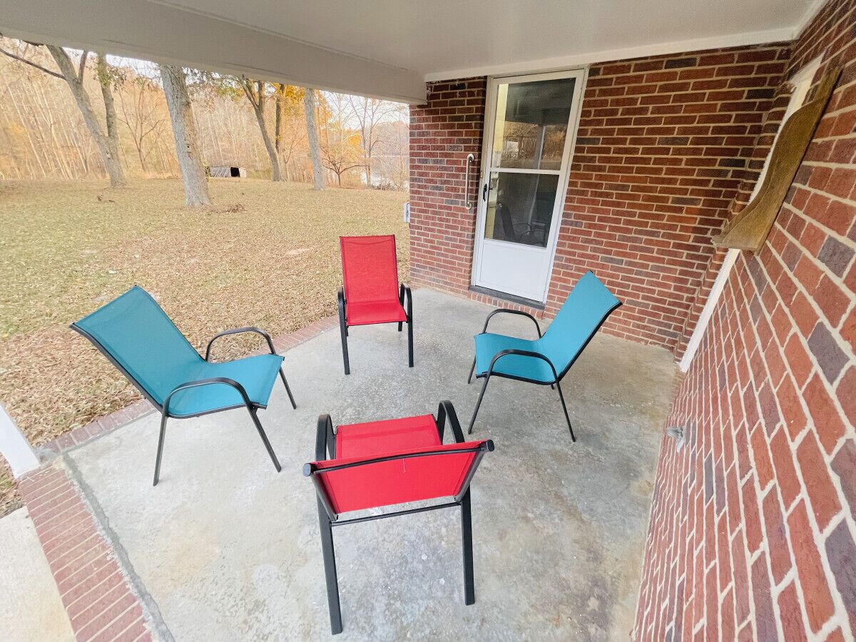 A covered patio with four chairs, one with a red cushion, and a brick wall.