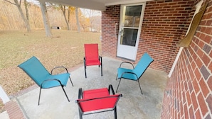 A covered patio with four chairs, one with a red cushion, and a brick wall. - Waterfront 3BR Home | Lake Views & Kayak Launch (Reidsville)